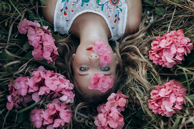 Una bella ragazza giace a terra con fiori sul viso e tra i capelli