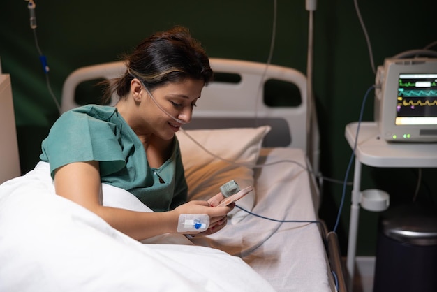 Una bella ragazza gioca a giochi sul suo telefono in ospedale passando il tempo mentre i medici la aiutano a sentirsi meglio