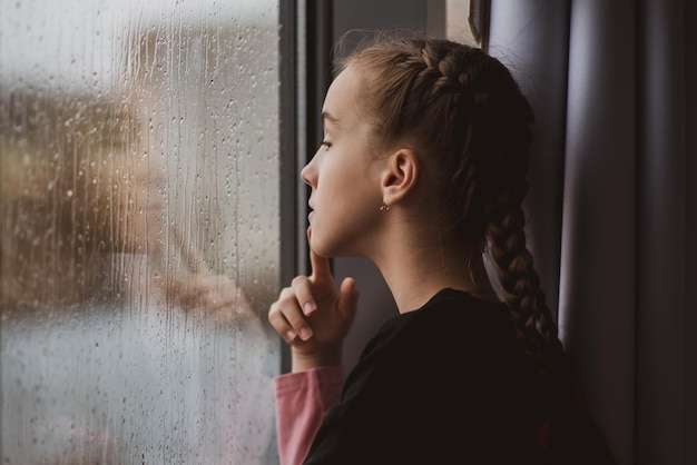 Una bella ragazza guarda fuori dalla finestra con la pioggia e sogna Atmosfera autunnale di pioggia