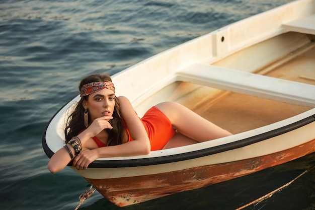 Una bella ragazza in costume da bagno rosso giace su una barca.