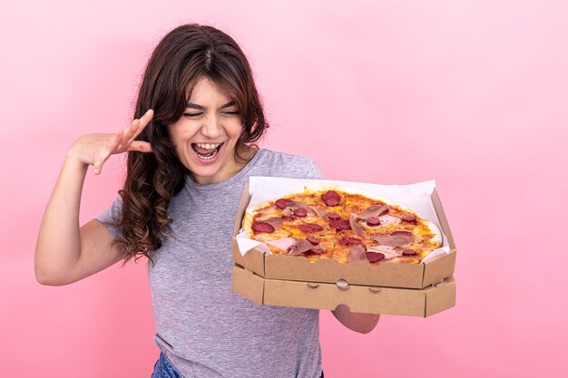 Una bella ragazza in possesso di una pizza in una scatola per la consegna su uno sfondo rosa.