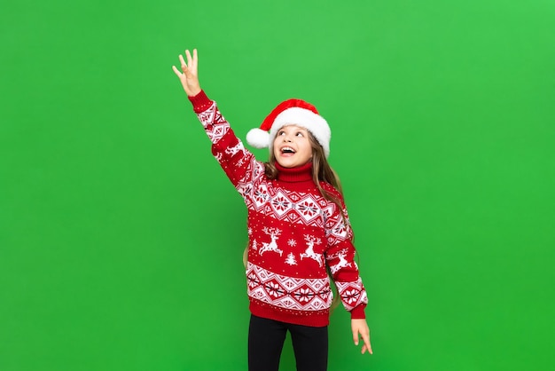 Una bella ragazza in un maglione rosso con le renne raggiunge il tuo annuncio su uno sfondo verde isolato Il concetto di Natale