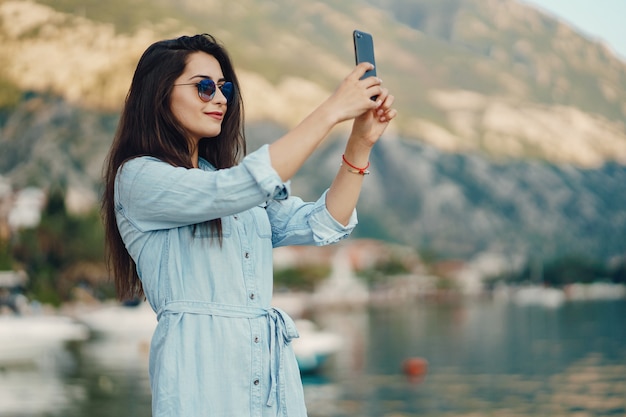 Una bella ragazza in un vestito blu che si siede vicino alle montagne e usa il telefono