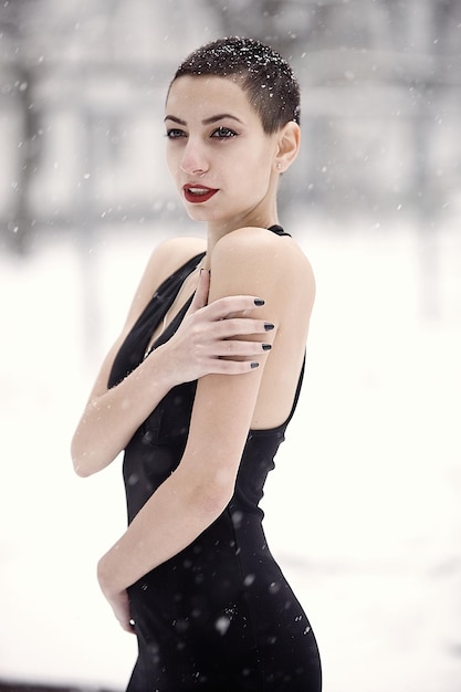 Una bella ragazza in un vestito nero su uno sfondo d'inverno nella foresta.