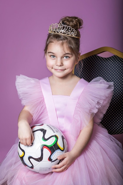 Una bella ragazza in un vestito rosa con un pallone da calcio e una corona