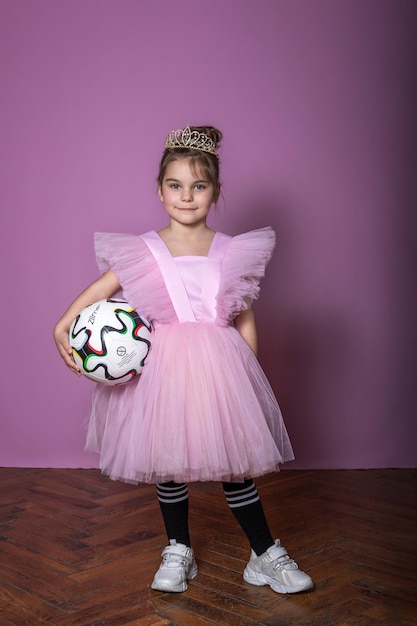 Una bella ragazza in un vestito rosa con un pallone da calcio e una corona