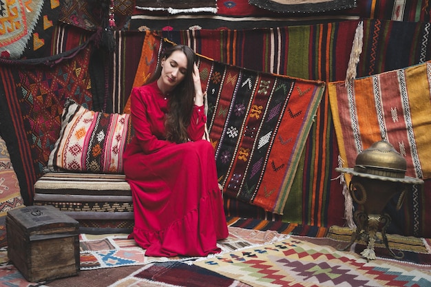 Una bella ragazza in un vestito rosso in un tradizionale interno turco con molti tappeti sul muro