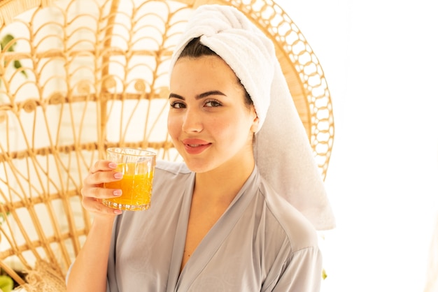 Una bella ragazza in vestaglia beve succo d'arancia. Saluta magnificamente la sua mattina prendendosi cura di se stessa