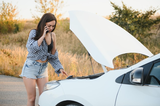 Una bella ragazza magra in camicia e pantaloncini sembra in un cofano aperto su una strada