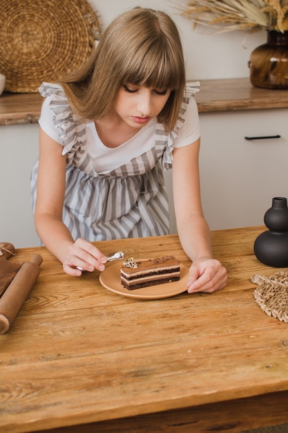 Una bella ragazza pasticciera con un grembiule a righe decora un dessert in cucina