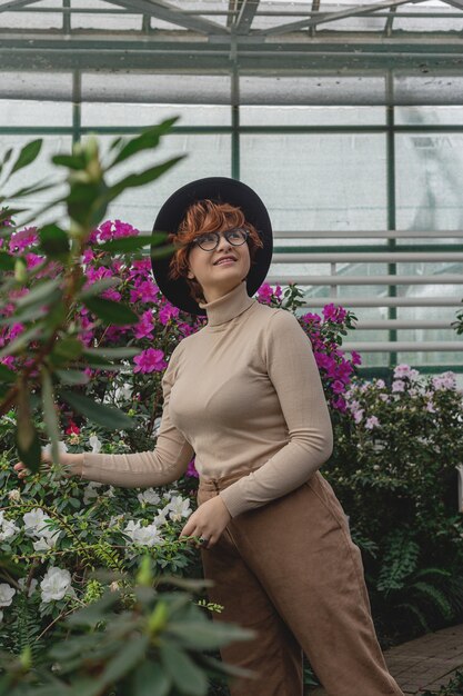 Una bella ragazza plus size con un cappello ride tra le piante verdi della serra