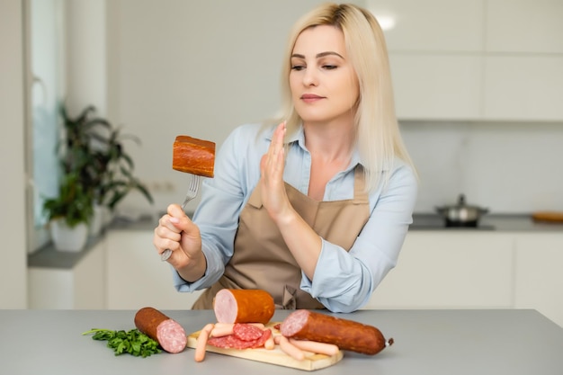 Una bella ragazza rifiuta le salsicce su uno sfondo neutro. Il concetto di vegetarianismo.