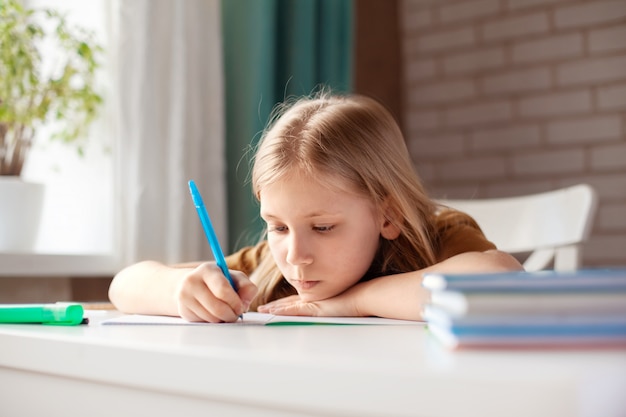 Una bella ragazza scrive con una penna su un quaderno. Il bambino esegue i compiti. Allenamento a casa, allenamento online