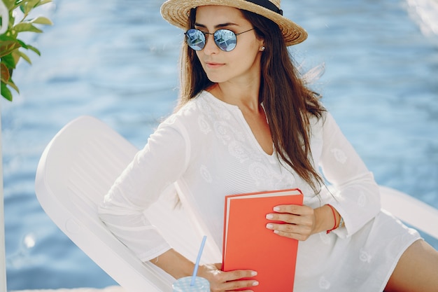 Una bella ragazza seduta su una terrazza estiva a bordo piscina con il libro