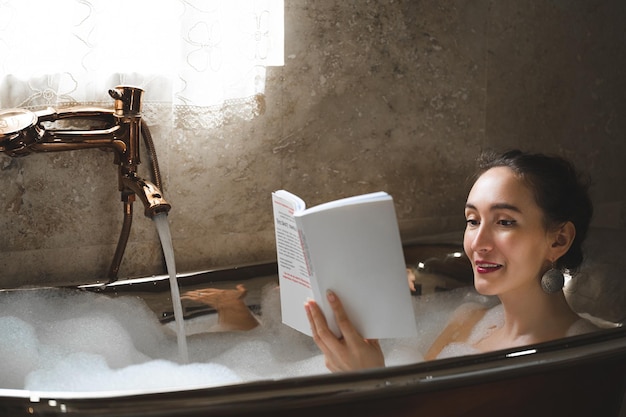 Una bella ragazza sexy in un bagno a bolle che legge un libro