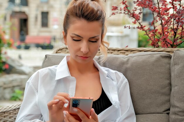 Una bella ragazza si siede in un caffè di strada e tiene un telefono nelle sue mani ragazza che ordina cibo per telefono