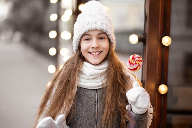 Una bella ragazza sorridente con caramelle cammina per l'atmosfera di Natale di Capodanno della città