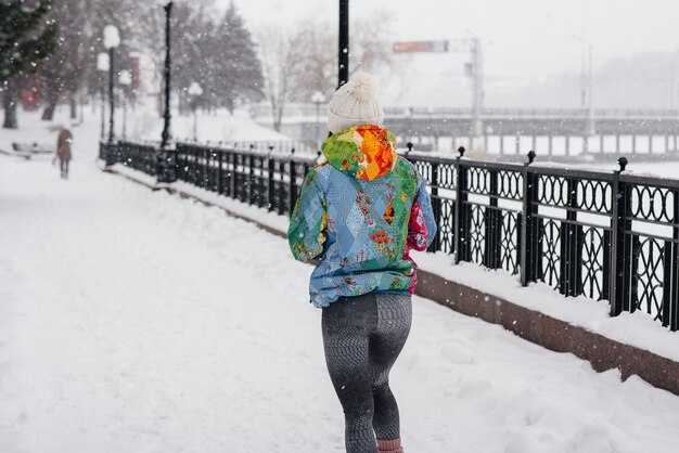 Una bella ragazza sta facendo jogging in una giornata gelida e nevosa. Sport, stile di vita sano.