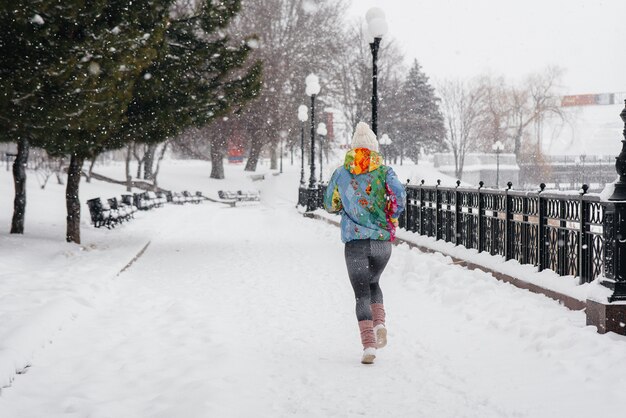 Una bella ragazza sta facendo jogging in una giornata gelida e nevosa. Sport, stile di vita sano.