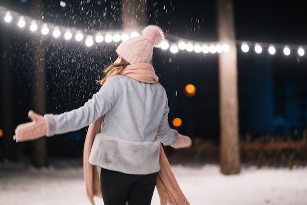 Una bella ragazza sta giocando con la neve Buon inverno nella foresta Luci festive della ghirlanda