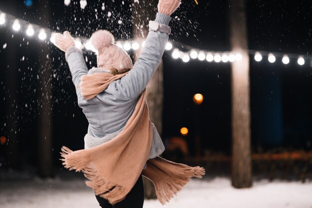 Una bella ragazza sta giocando con la neve Buon inverno nella foresta Luci festive della ghirlanda