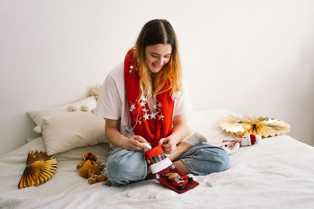 Una bella ragazza tiene in mano una calza di Natale e ne tira fuori qualcosa Design interno accogliente e confortevole Lavoro a casa Concetto di Capodanno e Natale