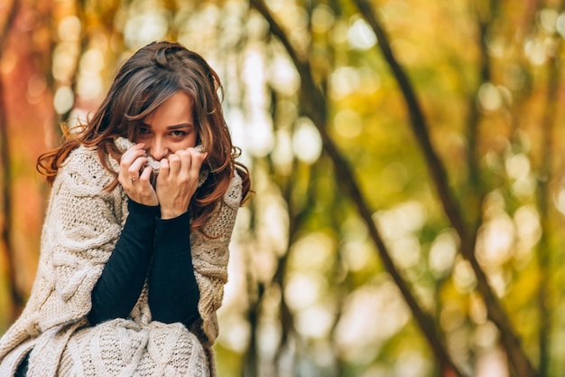 Una bella ragazza tiene le mani sul colletto di un maglione caldo nel parco in autunno