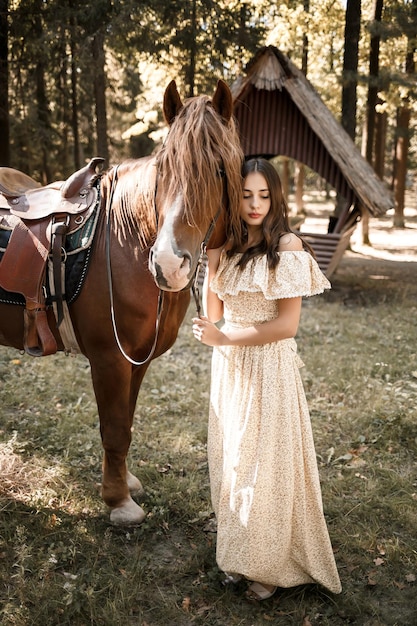 Una bella ragazza vestita con un vestito sta vicino a un cavallo nella foresta