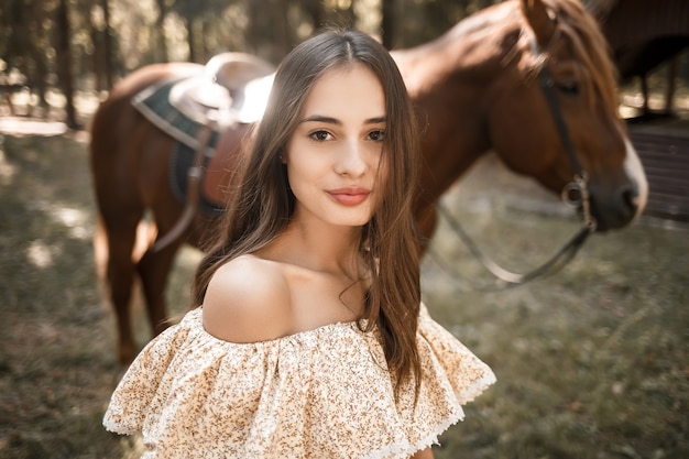 Una bella ragazza vestita con un vestito sta vicino a un cavallo nella foresta