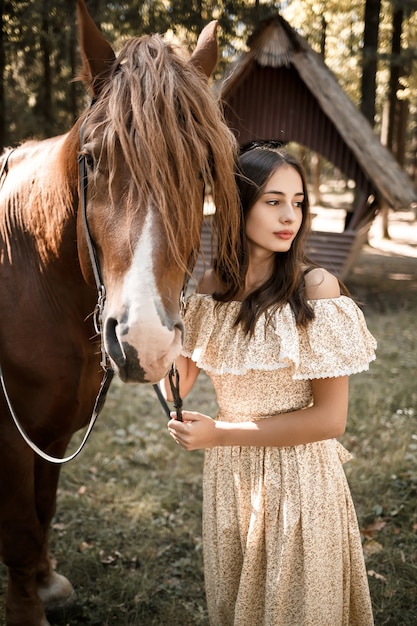 Una bella ragazza vestita con un vestito sta vicino a un cavallo nella foresta