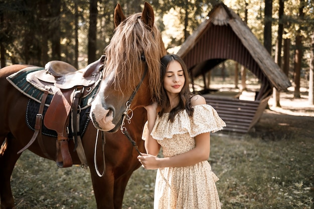 Una bella ragazza vestita con un vestito sta vicino a un cavallo nella foresta