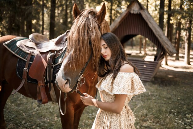 Una bella ragazza vestita con un vestito sta vicino a un cavallo nella foresta