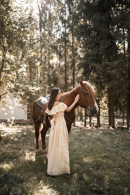 Una bella ragazza vestita con un vestito sta vicino a un cavallo nella foresta