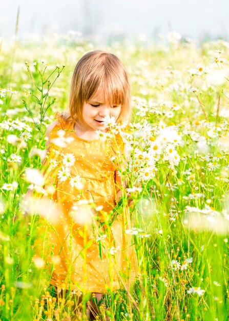 Una bella ragazzina con un vestito annusa fiori selvatici