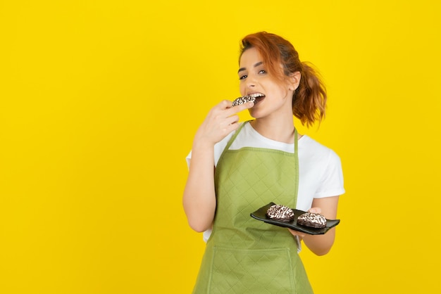 Una bella rossa che cerca di mordere una torta fresca sul muro giallo