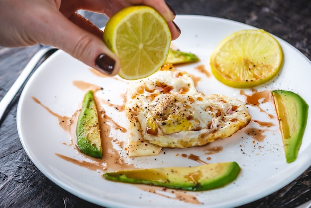 Una bella sana colazione romantica di uova fritte a forma di cuore con fette di avocado e limone