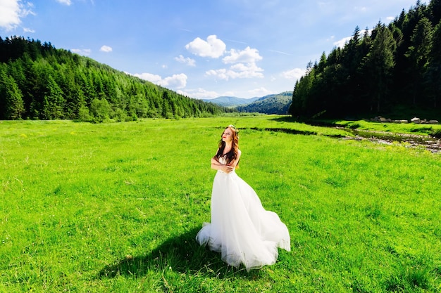 Una bella sposa dai capelli ricci in un lungo abito bianco di pizzo sta camminando sull'erba nel prato