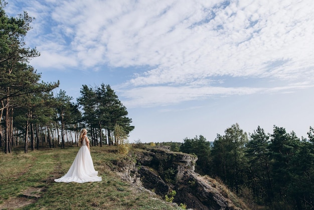 una bella sposa in abito bianco si erge sulla cima di una montagna