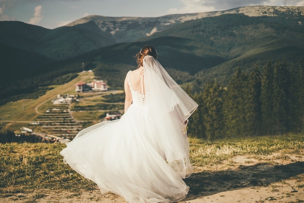 Una bella sposa in abito da sposa sta girando in montagna. Vista posteriore. Foto di alta qualità