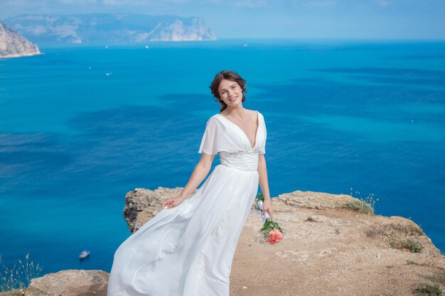 Una bella sposa in piedi sulla costa La sposa in montagna Matrimonio Romantica bella sposa in abito bianco in posa sullo sfondo del mare