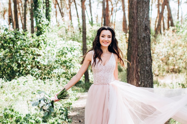 Una bella sposa in un delicato abito rosa all'aperto, la ragazza ha in mano un bouquet