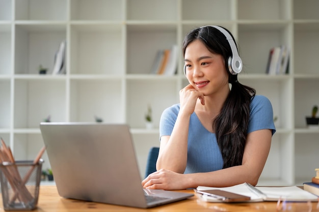 Una bella studentessa asiatica che indossa le cuffie e guarda lo schermo del suo laptop.