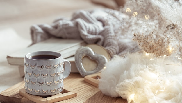 Una bella tazza con una bevanda calda sullo sfondo di cose accoglienti. Comfort domestico e concetto di calore.