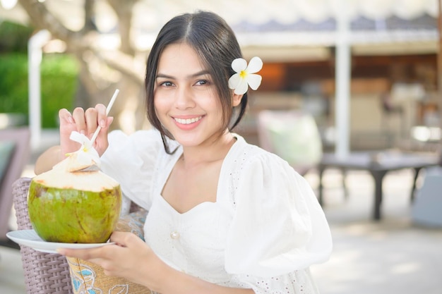 Una bella turista con fiore bianco sui capelli che beve cocco