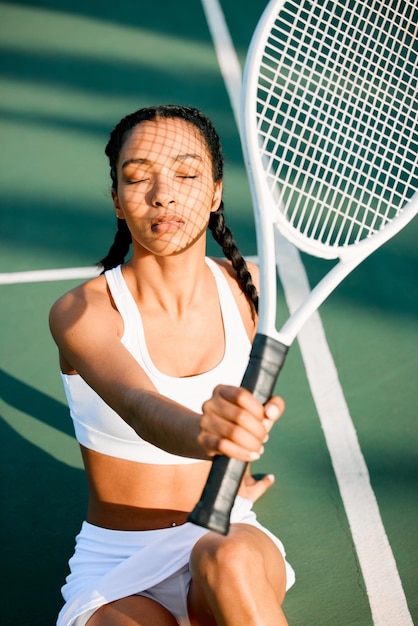 Una bellezza sul campo Inquadratura di una giovane donna sportiva che si protegge il viso dal sole con una racchetta da tennis su un campo