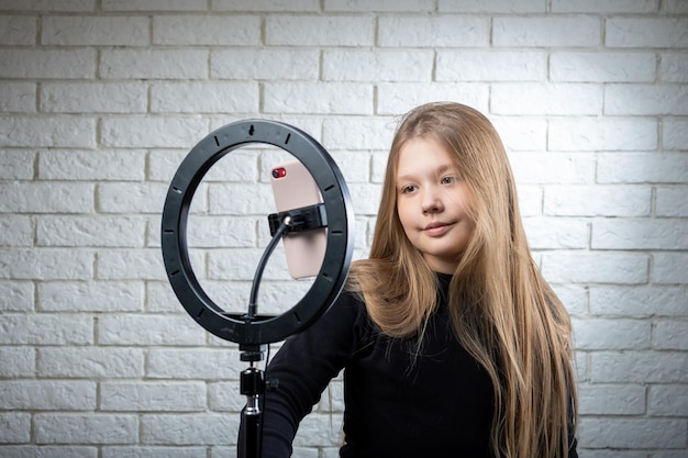 Una bellissima adolescente bionda sta trasmettendo in diretta Il video blogger ha una trasmissione in diretta Una lampada anulare e una telecamera durante una trasmissione in diretta di un video blogger