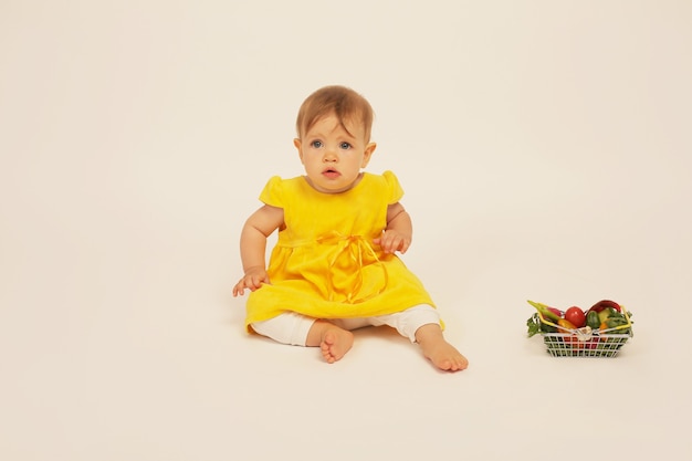 una bellissima bambina con un vestito giallo è seduta accanto a un piccolo cestino con le verdure