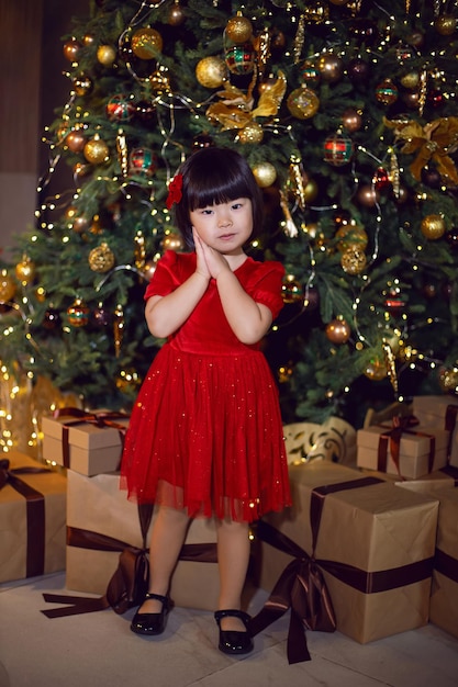 Una bellissima bambina coreana vestita di rosso si trova all'albero di Natale il giorno di Natale