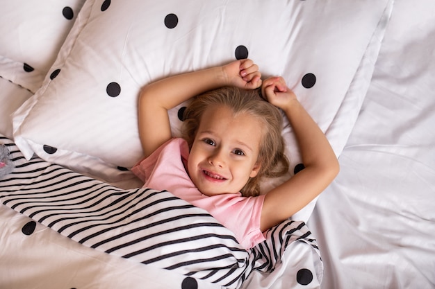 Una bellissima bambina in pigiama è sdraiata su lenzuola di cotone sul letto