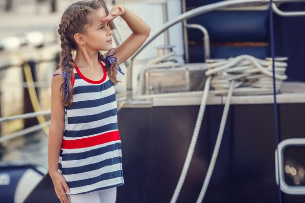 Una bellissima bambina in stile marinaro sullo sfondo di barche e yacht.